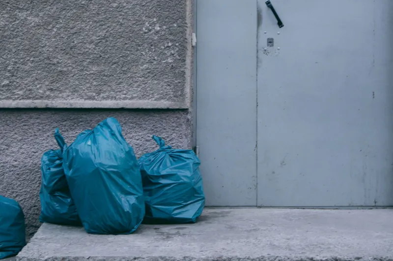 Blue garbage bags stacked beside a metal door on concrete steps